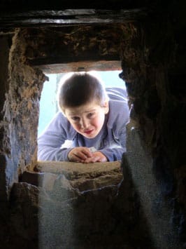 Child peers through one end of a tunnel formed by rocks.