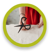 A person holds a pair of scissors over cloth on a flat surface.