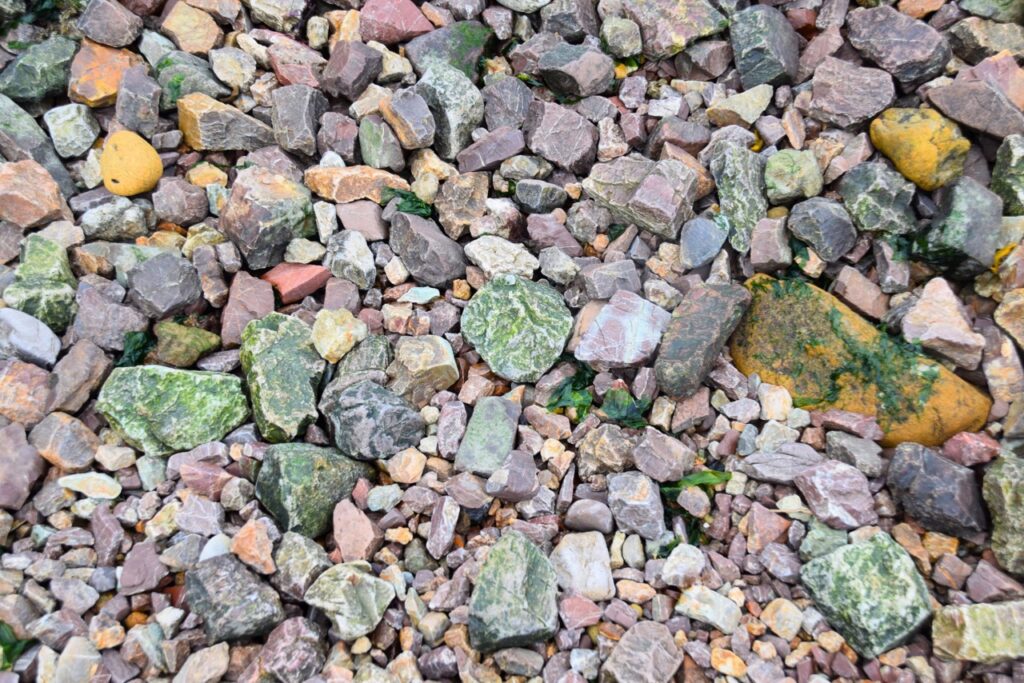 A photo of rocks that make up the Rocky Beach. The rocks are mostly fist-sized, and come in a variety of colors including green, red, yellow, gray, black, and white. Many rocks include multiple colors mottled together. 