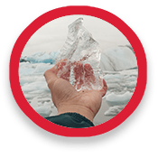 A hand holds up chunk of jagged ice, with icebergs in the background.
